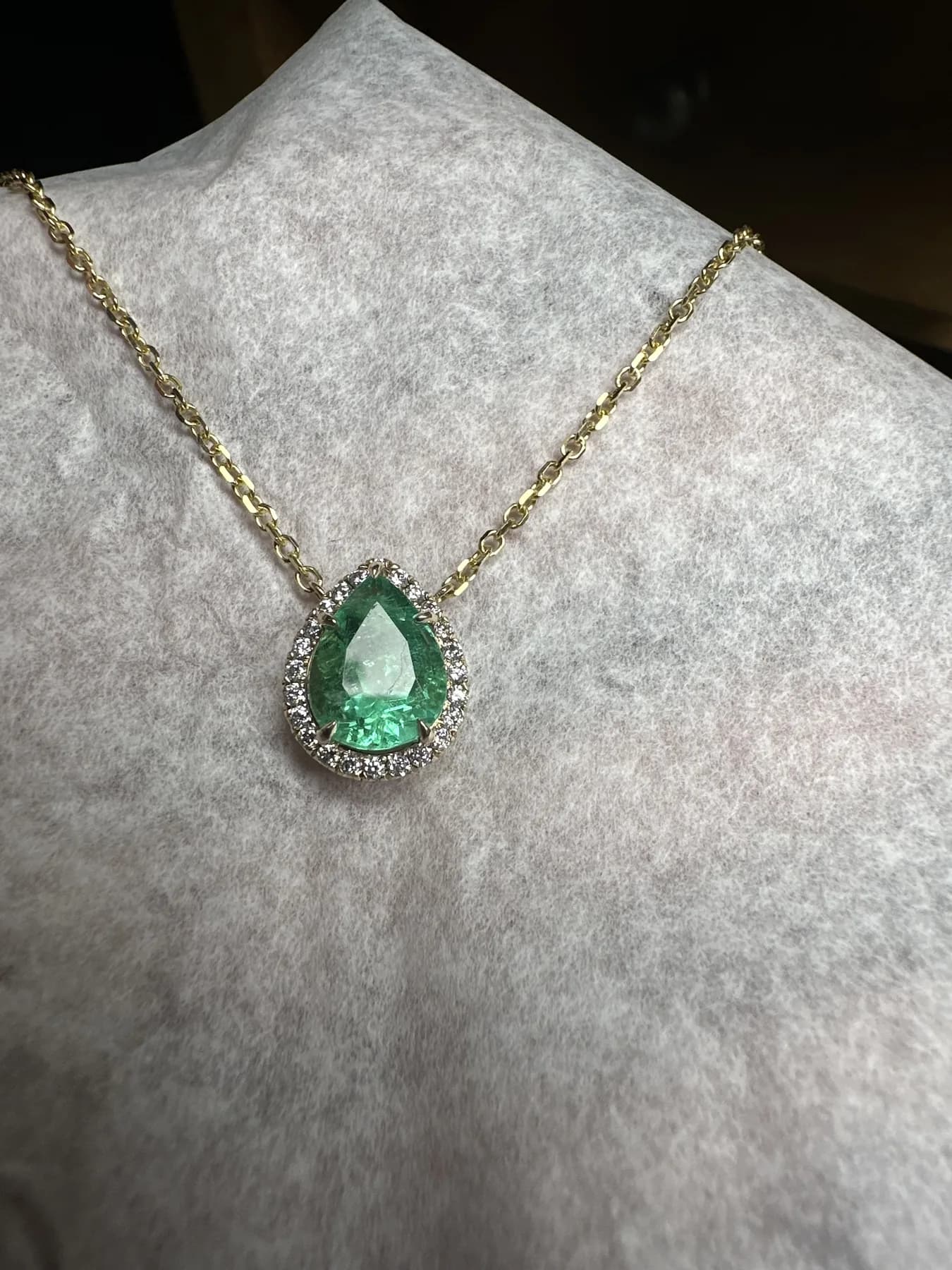 Pear-shaped green gemstone pendant with a halo of small colorless stones on a yellow-toned chain